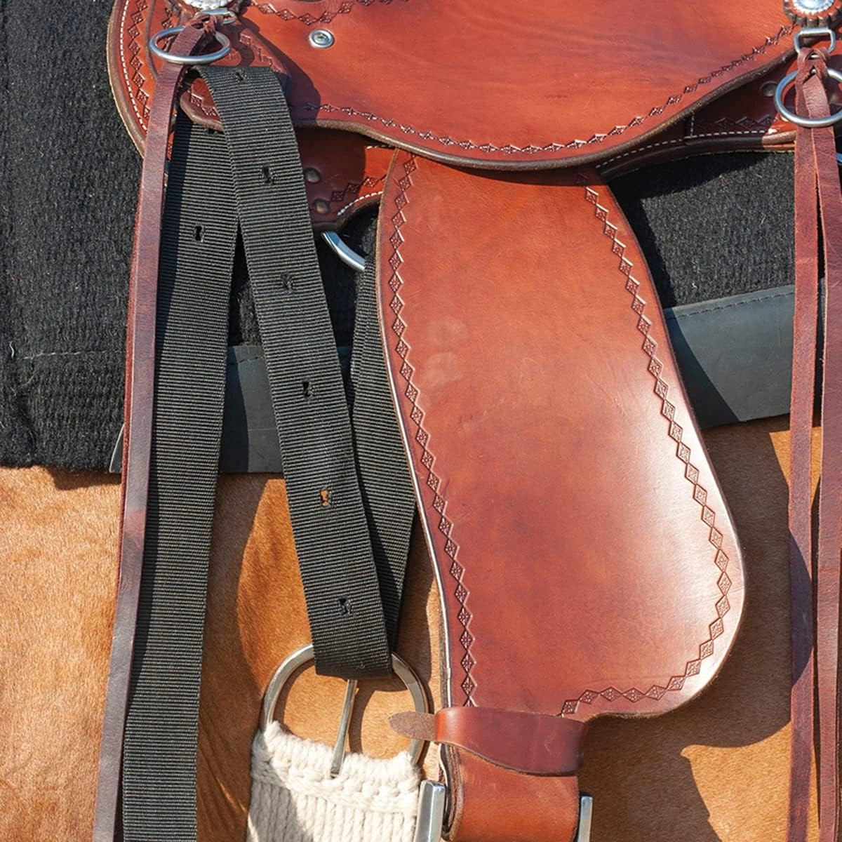 Close-up of a brown leather saddle with black straps on a textured surface