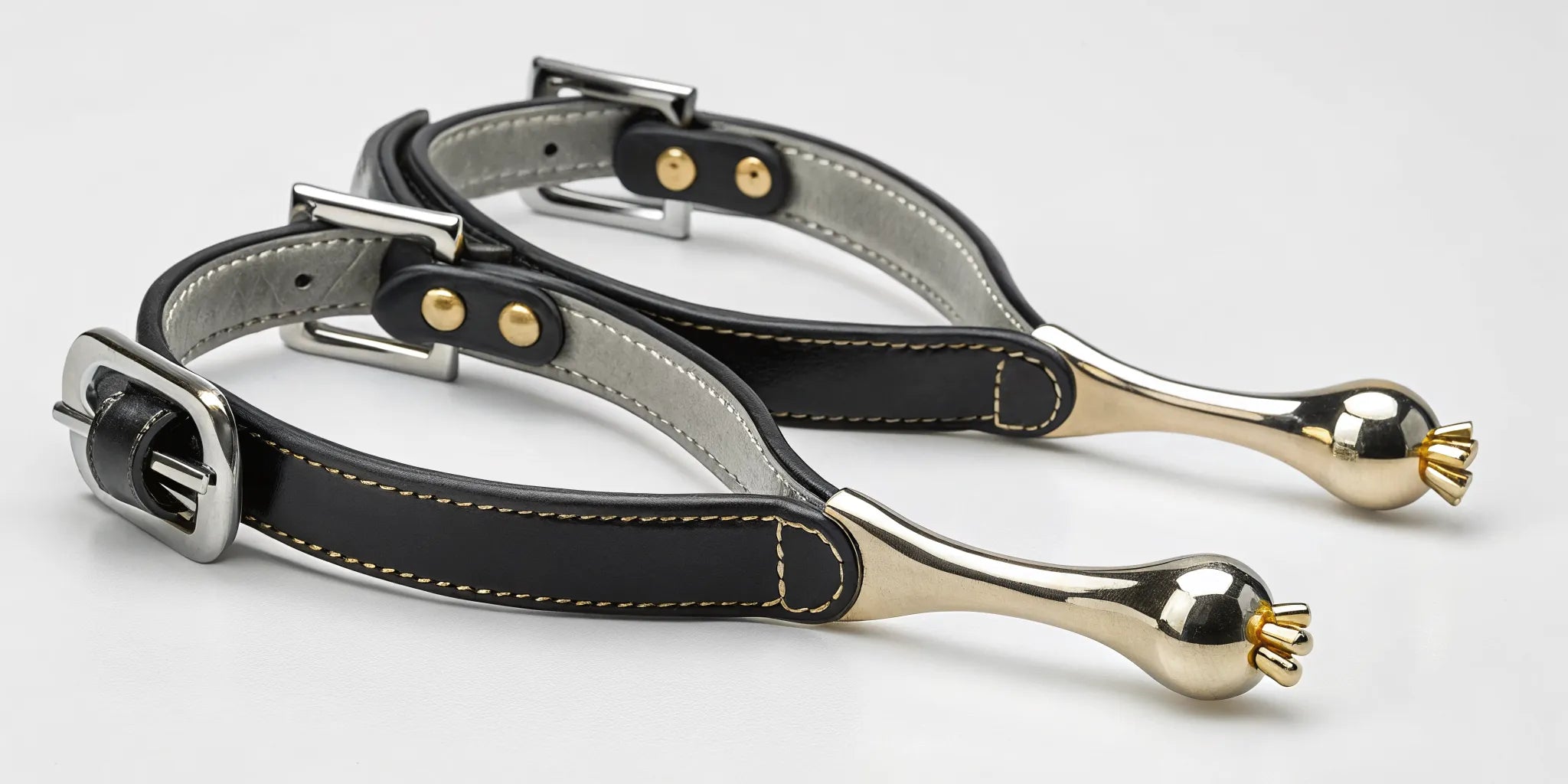 A pair of English spurs with gold rollers and black leather straps.