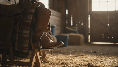 Rider boot resting in a stainless steel horse stirrup beside a Western saddle
