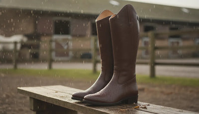 Elegant waterproof women's riding boots with a heel displayed in soft rain outside a barn