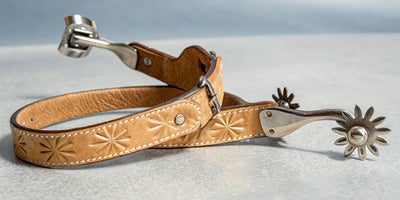 A pair of Western spurs with tooled leather straps and spinning rowels.