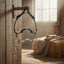 Myler MB 06 Combination Bit (sweet iron, low port, copper inlay) hanging on a wooden peg in a sunlit barn. Features a black leather and rope headstall, with a hay bale, blanket, and gloves in the background.