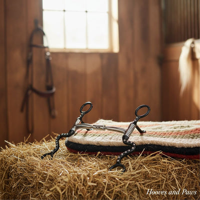 Myler Black Steel Seven Shank Comfort Snaffle Wide Barrel MB 02 horse bit with decorative studs, resting on a striped saddle pad and hay in a barn.