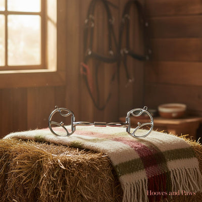 Myler 5" Western Dee with Hooks and Comfort Snaffle Wide Barrel MB 02 horse bit on a striped blanket over a hay bale in a sunlit barn with hanging tack.