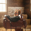Black Cashel Fleece Tush Cushion on a brown leather western saddle in a rustic, sunlit barn setting with hay.