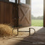 Pony size Myler stainless steel Dee snaffle bit with a single-jointed mouthpiece rests on a sunlit wooden stable floor. Next to straw, an open stable door reveals a green pasture.