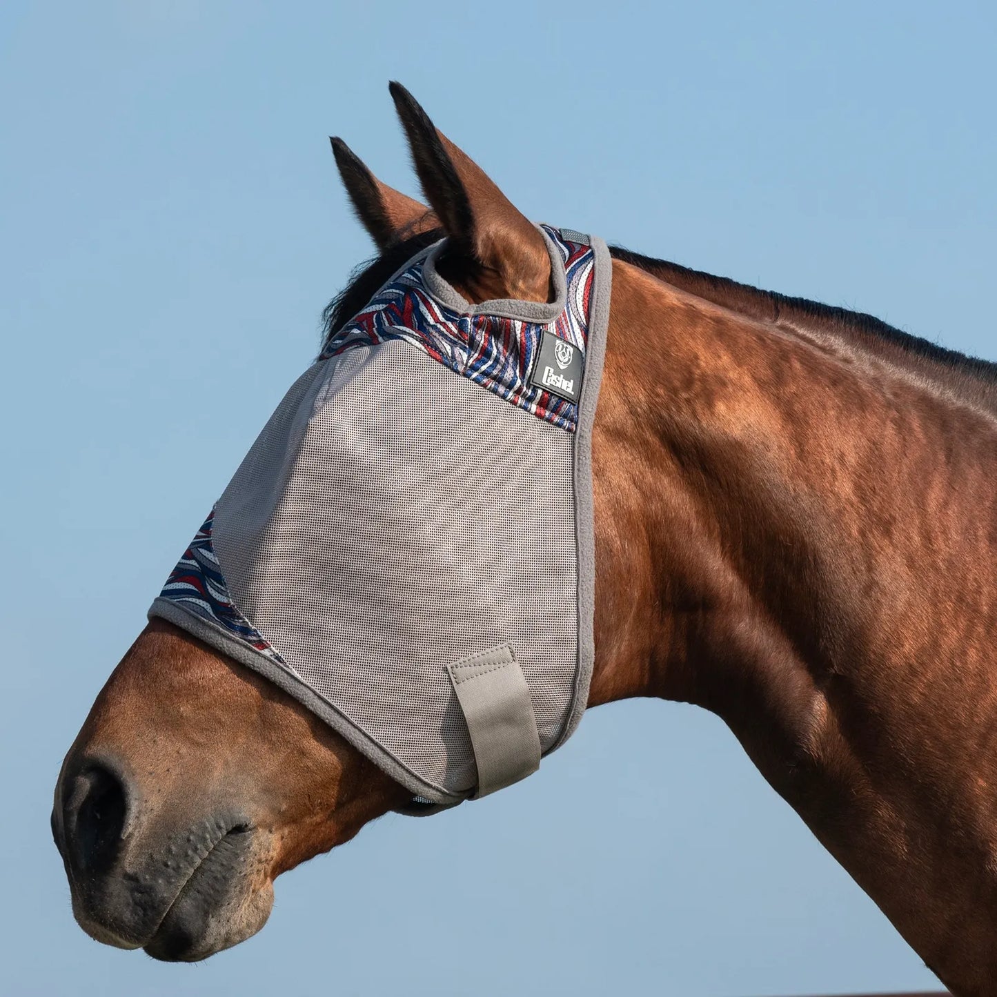 Cashel Crusader Fly Mask in the American Wave & Pluma pattern shown on a bay horse. This high-quality horse fly mask features a breathable grey mesh screen for UV protection, soft fleece padding to prevent rubbing, and a secure hook-and-loop closure. The patriotic red, white, and blue patterned trim adds a stylish touch to essential fly protection. Perfect for keeping your horse comfortable and insect-free during turnout. Durable and comfortable equestrian gear for summer.