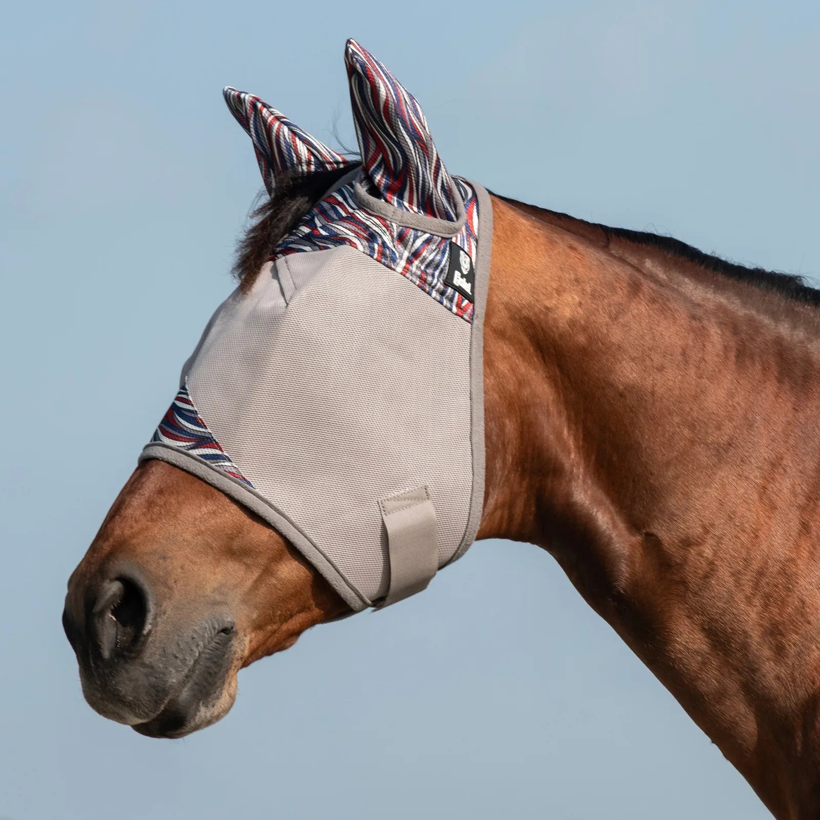 Cashel Crusader Fly Mask in American Wave & Pluma design on a bay horse. This premium grey mesh horse fly mask features patriotic red, white, and blue wavy patterns on the ears and trim. Engineered for ultimate horse fly protection and UV defense, it keeps pests away from eyes and ears while ensuring a comfortable, secure fit for turnout. High-quality equestrian gear for effective fly control and summer sun protection.