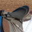 Black Cashel English Tush Cushion seat saver fitted onto a brown leather English saddle. This high-density foam saddle cushion provides ultimate rider comfort and shock absorption for long hours in the saddle. It features adjustable straps for a secure fit and is shown on a horse with a white quilted saddle pad, making it a must-have accessory for trail riding or training to prevent soreness and fatigue.