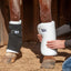 White Cashel No Bow Bandage Wrap being applied to a horse's leg for superior cushioning and support. A person's hands hold the thick, quilted white wrap in place, while the adjacent leg shows a black bandage secured over a similar wrap. Ideal for equine leg protection, injury recovery, or shipping, these breathable and soft wraps prevent pressure points and ensure maximum comfort. Perfect for horse trailering and stall rest.