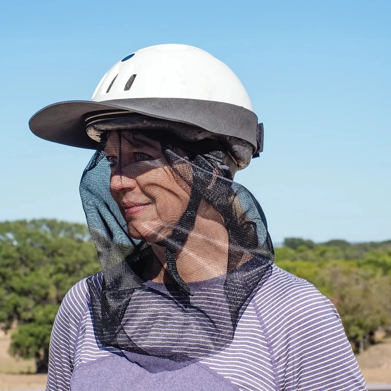 Cashel Quiet Ride Fly Mask for horse riders, featuring a black fine-mesh veil that shields the face and neck from biting insects and flies. Shown attached to a white equestrian helmet with a wide sun brim, this lightweight mesh protector provides clear visibility and breathable fly protection. A must-have equestrian accessory for comfortable, bug-free trail riding and insect protection during summer rides.