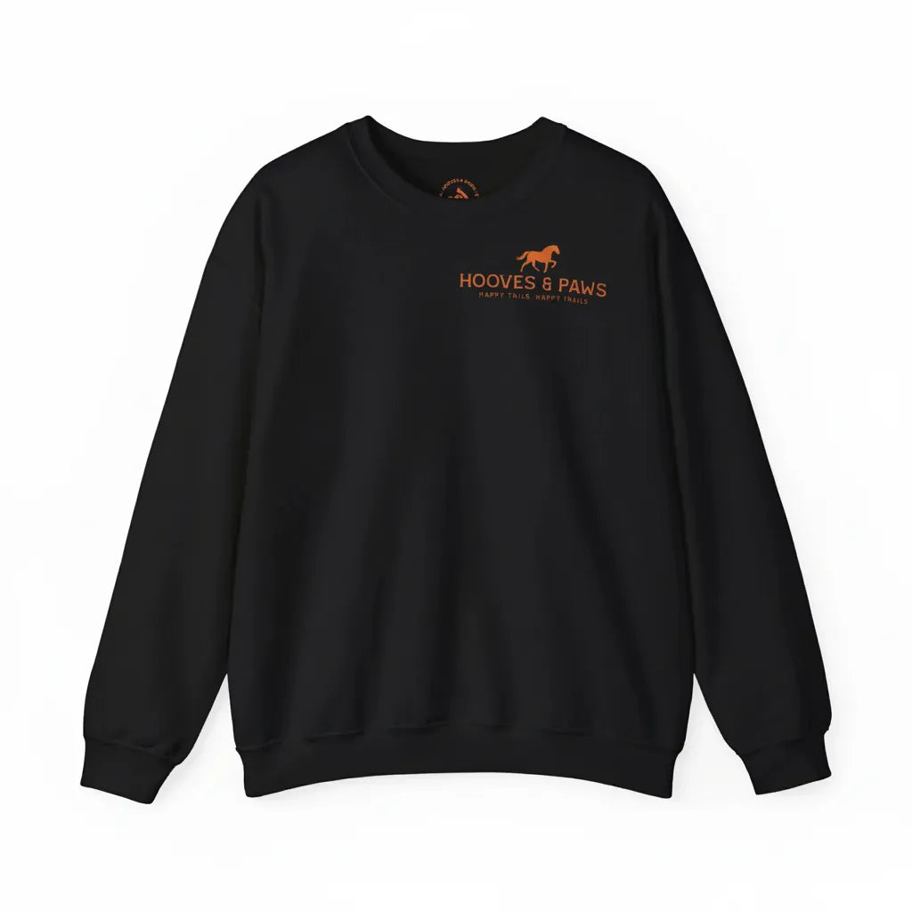 Black crewneck sweatshirt featuring a small orange equestrian logo on the left chest. The minimalist design includes a trotting horse icon with "HOOVES & PAWS" and the tagline "HAPPY TAILS, HAPPY TRAILS" printed in vibrant orange. This 8.0 oz medium-heavy blend pullover offers a cozy, classic fit for horse lovers and riders, making it a stylish and comfortable choice for casual stable wear or everyday equestrian fashion.