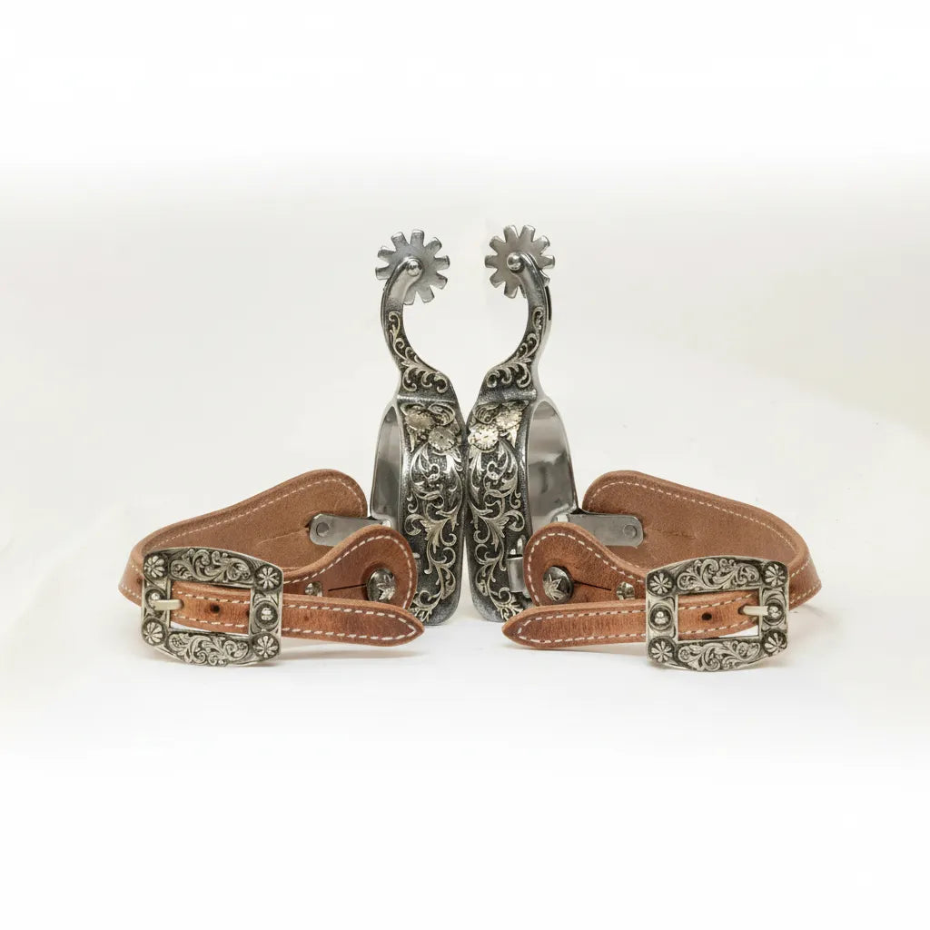 Professional's Choice 50th Anniversary PC 50 Western Spur Set for men. These gunmetal finish spurs feature an elegant swan neck, 6-point rowel, and intricate floral scroll engraving. Accompanied by premium brown leather straps with matching ornate silver buckles, these 3 1/4" width spurs offer a classic, high-performance look for professional riders and western enthusiasts.