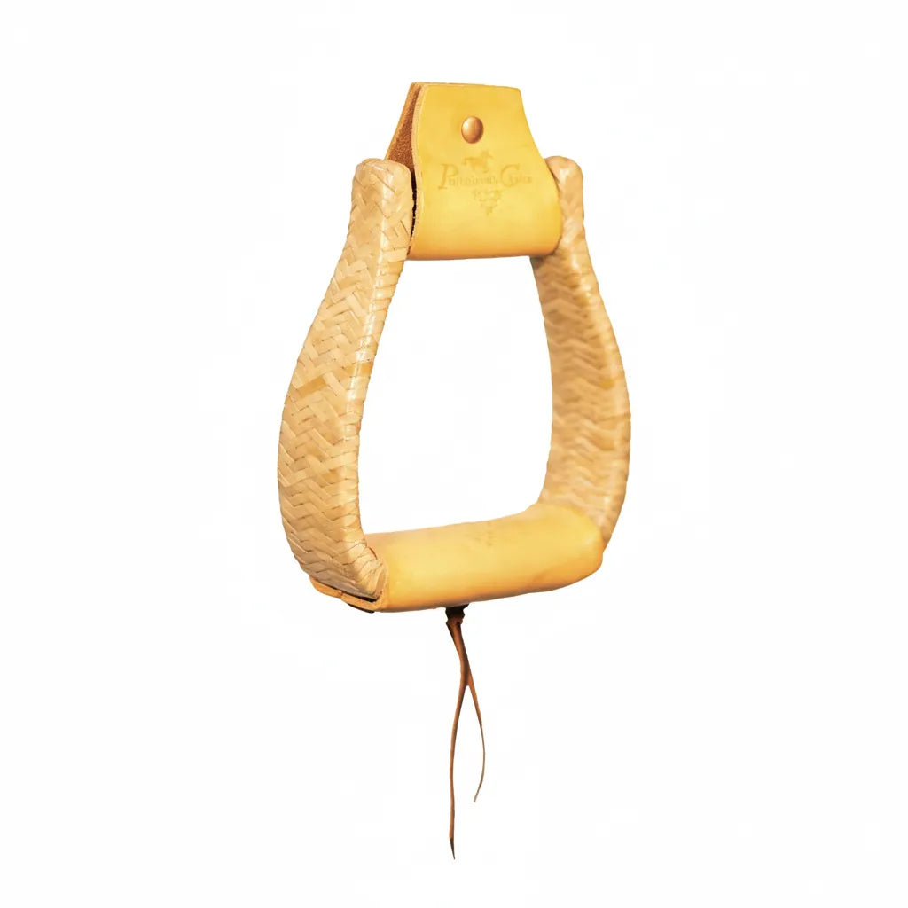 Professional's Choice Rawhide Braided Western Slanted Stirrups in natural tan. These ergonomic Vaquero-style stirrups feature intricate rawhide braiding along the sides and a wide, comfortable leather tread. The neck is finished with a stamped logo and a copper rivet, while a classic leather tie adds an authentic touch. Perfect for western saddle upgrades, these high-quality stirrups offer traditional style and enhanced comfort for trail or ranch riding.
