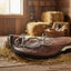 Myler Kimberwick MB 36 horse bit, stainless steel with a ported barrel mouthpiece, resting on a brown leather saddle pad in a rustic barn setting with straw.