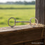 Myler Eggbutt Snaffle bit for dressage and eventing on a rustic wooden railing with green field background.