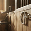 Myler 27PB Stainless Steel English Dee with Hooks horse bits hang on a wooden stable wall, with sunlit hay bales in the blurred background.