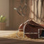 Myler 02 Stainless Steel English Dee with Hooks bit in the foreground, leaning against a brown English saddle and blue saddle pad, all on hay on a wooden floor in a sunlit equestrian stable.