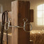 Myler 5 inch 02 Stainless Steel Medium Baucher bit (#89-41025) hanging on a rustic wooden stable post, with a blurred leather bridle, reins, and hay bale in a sunlit barn background.