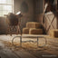 Silver Myler Medium Dee snaffle horse bit on a straw-covered wooden barn floor, with a saddle, hay bales, and a horse in a stable in the background, depicting an equestrian setting for horse communication and comfort.