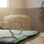 Myler Bridoon SS Low Port Mullen Barrel Bit #89-40067, a gleaming stainless steel horse bit, resting on a green plaid blanket on a rustic wooden table inside a sunlit barn with dust motes, hay bales, and a horse in a stall.