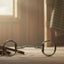 Myler Eggbutt with Hooks stainless steel Mullen Barrel Low Port MB 06 5 1/2 inch horse bit on a weathered wooden floor, next to a brown leather bridle on a pile of straw, in a sunlit barn interior.
