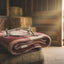 Myler 5 1/2" Weymouth Wide Ported Barrel Bit MB 16PB resting on a folded red and cream plaid blanket atop a wooden barrel, in a rustic barn setting with hay bales and sunlit stable doors.