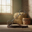 Shiny Myler MB 10 French Link Snaffle horse bit resting on a brown leather strap on a wooden stable floor, with a blurred hay bale, wooden bucket, and sunlit window in the background.