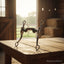 A Myler MB 36 Sweet Iron Forward Tilt Ported Barrel Curb Bit stands upright on a rustic wooden table inside a sunlit barn, with an open door revealing a green field and hay bales in the background.