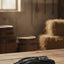 Myler Roeck ROECK Grip LITE black riding glove, featuring textured fabric and a snap closure, resting on a rustic wooden table. A blurred sunlit barn interior with hay bales, barrels, and horse tack is in the background.