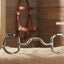 Myler 33 Eggbutt with Hooks 5 1/2" horse bit, shiny stainless steel, on a hay bale in a rustic barn setting with equestrian gear.