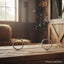 Myler MB 02 Loose Ring Snaffle Bit, 6-inch size with copper inlay, on a rustic wooden stable table. A blurred background reveals a sunlit barn interior with hay and hanging equestrian tack.