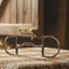 Myler 4 1/2 inch English Pony Dee horse bit with hooks, stainless steel mullen barrel low port #89-22063, resting on a textured brown fabric with blurred hay and a wooden stable door in the background.