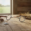 Myler Eggbutt Snaffle horse bit, 5-inch with copper inlay, lying on a rustic wooden stable table with scattered hay and brown leather tack, a green field visible through a window in the background.