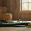 Myler MB 33 Dee Snaffle horse bit in stainless steel with a ported barrel and copper inlay, displayed on a green equestrian blanket with a leather strap and brush in a sunlit wooden barn with hay bales.