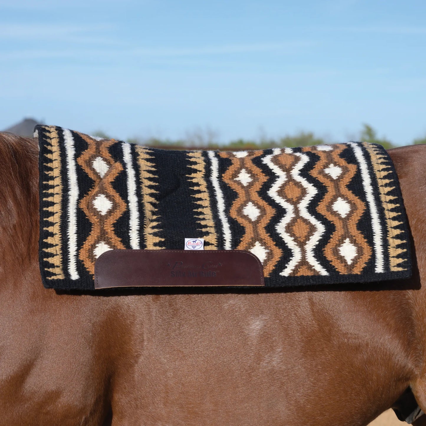 Professional's Choice Comfort-Fit SMx Air Ride Saddle Pad featuring a bold Southwestern geometric pattern in black, chocolate brown, and tan. This premium western saddle pad features durable leather wear leathers and a contoured spine for an anatomical fit and superior shock absorption. Perfect for horse lovers looking for stylish, high-performance western tack, shown on a horse against a clear blue sky. Ideal for performance, training, or trail riding.