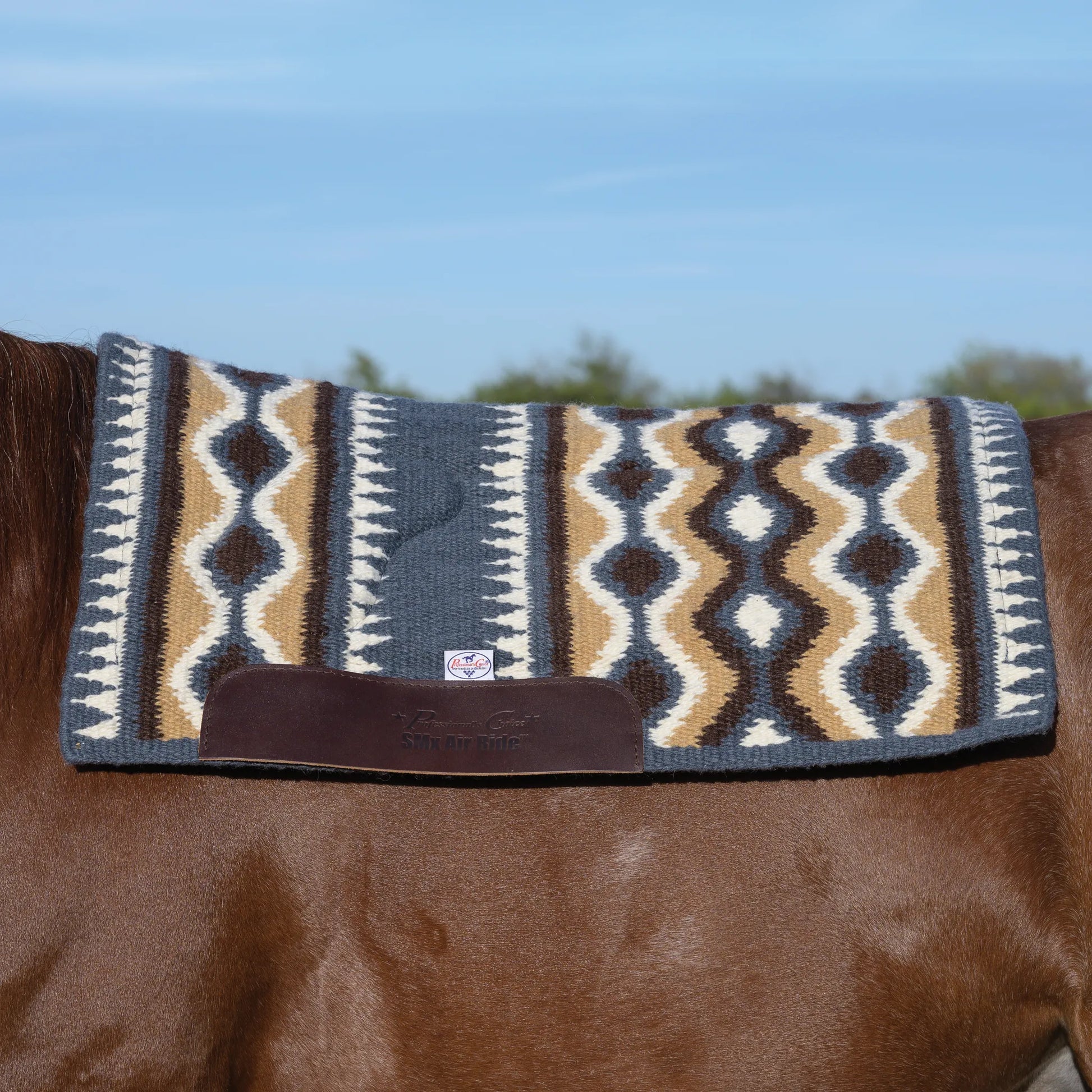 Professional's Choice Comfort-Fit SMX Air Ride Western Saddle Pad on a chestnut horse. Featuring a stylish Southwestern geometric pattern in slate blue, tan, and chocolate brown, this orthopedic saddle pad includes reinforced leather wear leathers and breathable core technology. A high-performance choice for western riders seeking maximum comfort and impact protection during trail riding or competition.