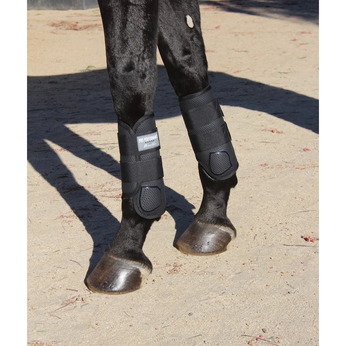 Professional's Choice Pro Performance Elite XC Boots in black, front pair, shown on a dark horse. These breathable equestrian boots feature a honeycomb TPU strike guard for superior impact protection and ventilated mesh to prevent overheating. Designed for cross-country and eventing, these medium-sized boots offer a secure, contoured fit with durable straps for high-performance horse leg protection.