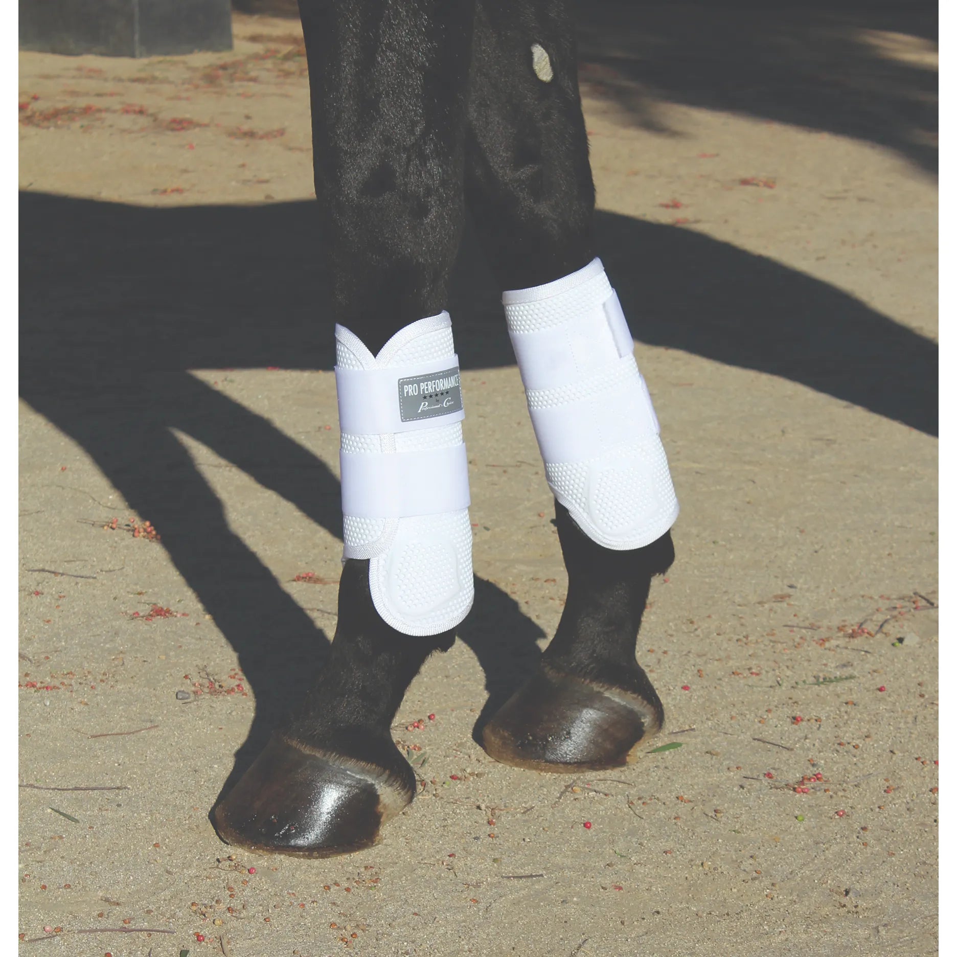 Professional's Choice Pro Performance Elite XC Boots in white, front pair, shown on a black horse. These medium-sized horse boots feature a breathable, shock-absorbing design with a textured protective shell and secure wrap-around straps. Ideal for cross-country jumping and high-impact equestrian activities, offering superior leg protection and a comfortable, anatomical fit for your horse.