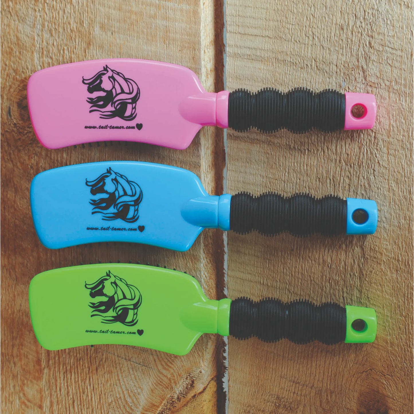 Professional’s Choice 909 Curve Brushes in vibrant pink, blue, and neon green. These ergonomic horse grooming tools feature a unique curved head and a black ribbed, non-slip handle for a secure grip. Branded with a horse logo and 'Tail Tamer,' these stylish brushes are essential equestrian supplies for grooming manes and tails. Shown on a rustic wood background, these assorted color brushes are a must-have for any horse owner's grooming kit.