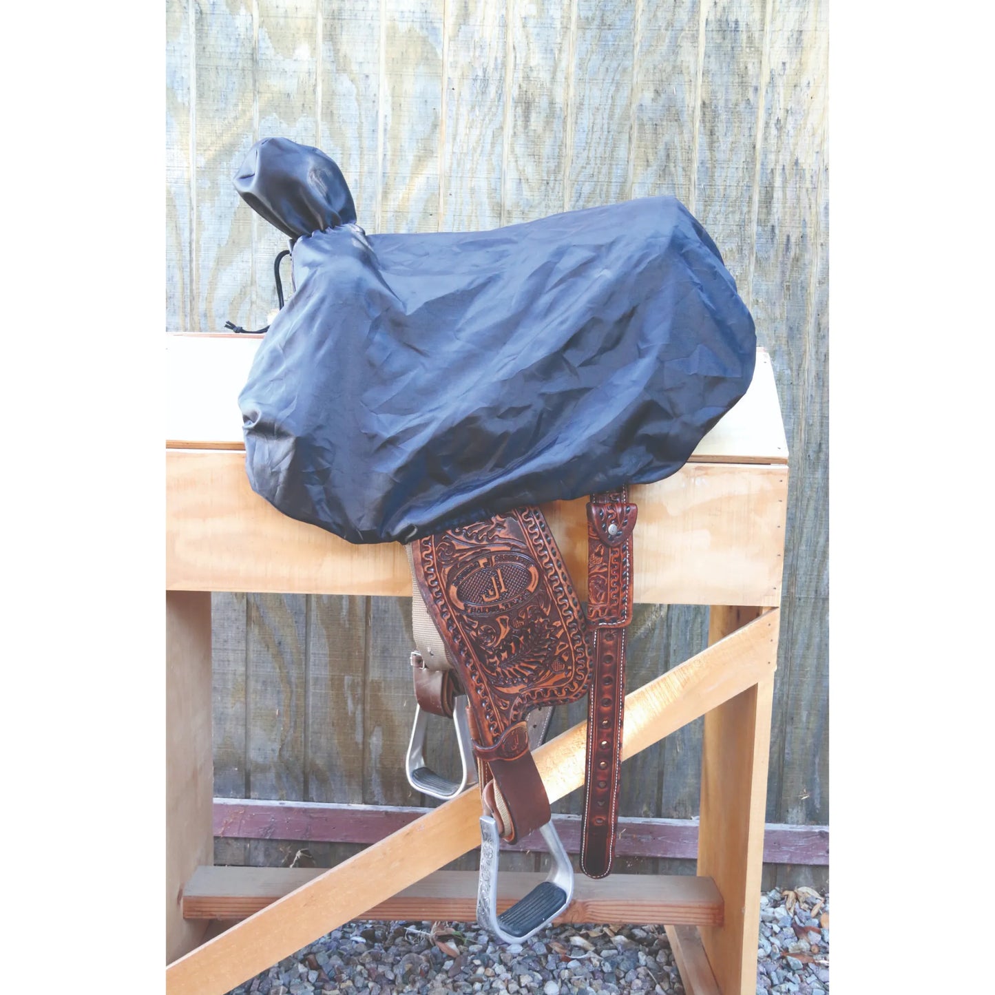 Professionals Choice Black Western Saddle Cover draped over a detailed leather saddle on a wooden stand. This durable, water-resistant cover protects the seat, cantle, and horn from dust, debris, and scratches. The sleek black material ensures a snug fit, while the tooled leather fenders and silver stirrups remain visible below. Ideal equestrian gear for preserving high-quality western saddles in the tack room or during travel.