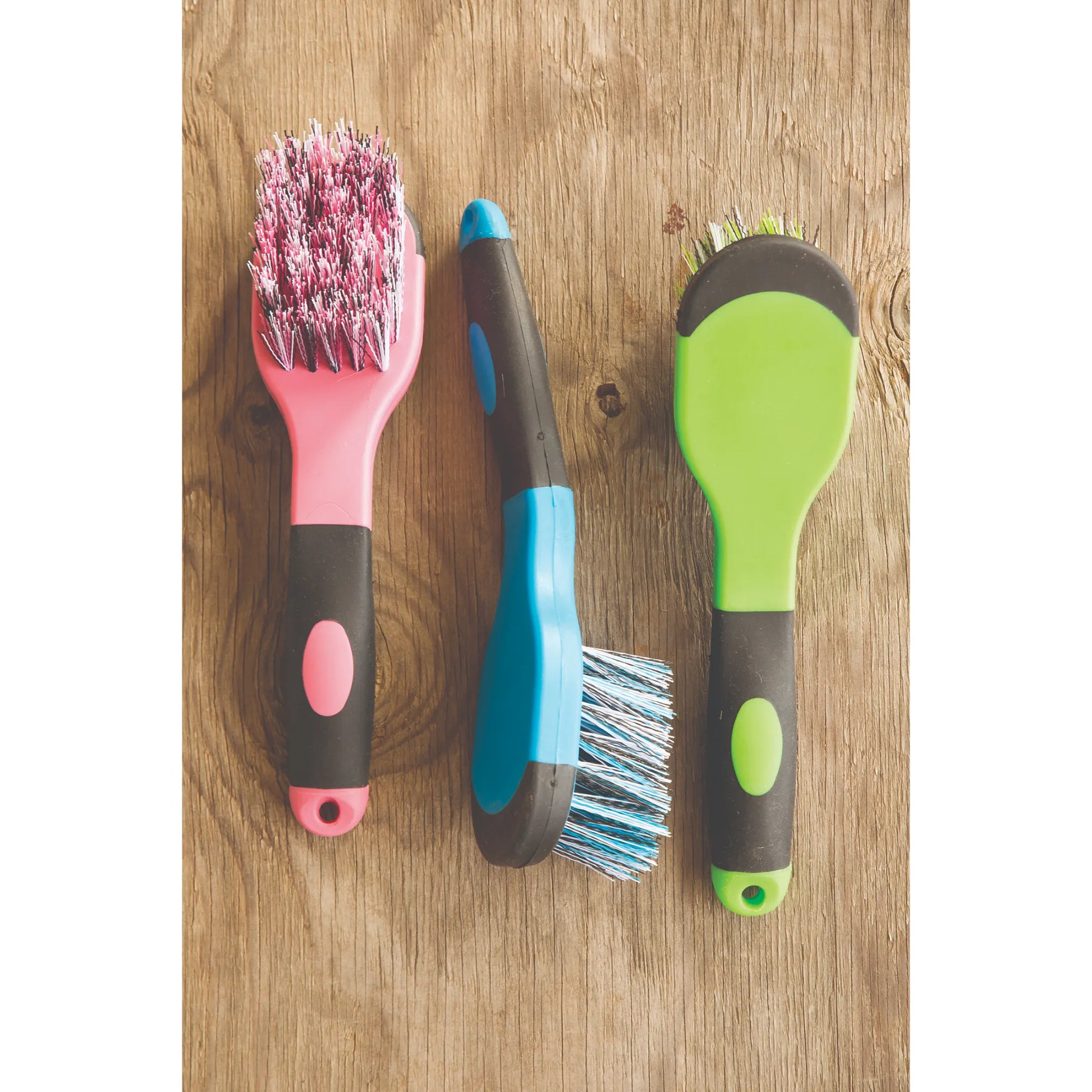 Professionals Choice Soft Touch Bucket Brushes in vibrant pink, blue, and green, displayed on a rustic wooden background. These equestrian grooming tools feature an ergonomic, non-slip grip handle and durable synthetic bristles specifically designed for heavy-duty cleaning of stable buckets and gear. A colorful and practical addition to any horse grooming kit or barn organization setup.