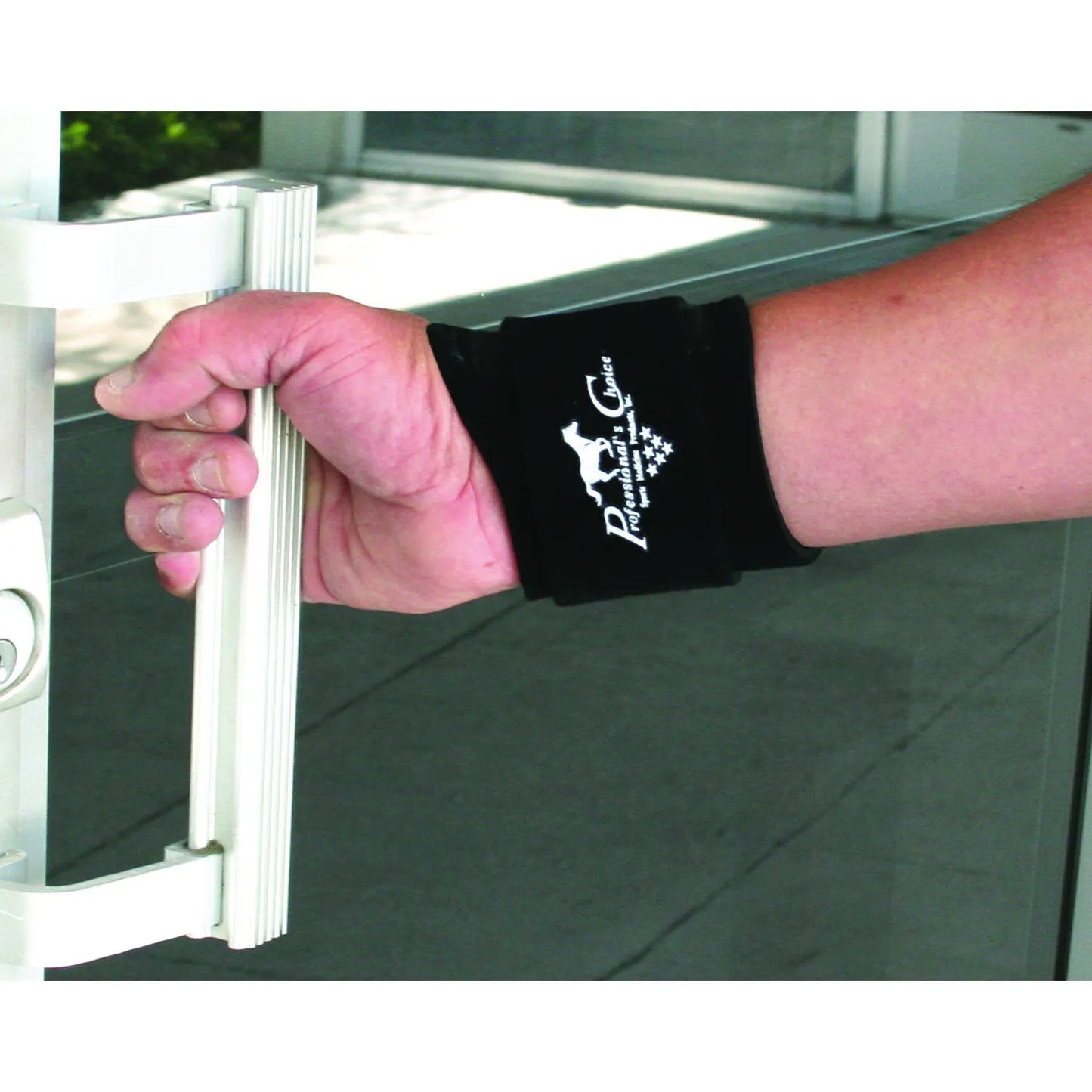 Professionals Choice Wrist Compression Wrap in black, shown worn on a person's wrist for support while gripping a handle. This adjustable wrist support wrap features a white Professional's Choice logo and provides firm compression for pain relief, carpal tunnel, and sports injury recovery. The sleek, low-profile design allows for full hand mobility while stabilizing the joint, making it ideal for athletes or daily use to prevent strain.