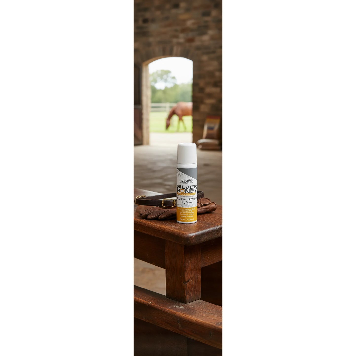 Absorbine Silver Honey Rapid Wound Repair Maximum Strength Dry Spray on a rustic wooden bench with leather tack. In the background, a horse grazes in a green field through a stable door. This medical-grade spray for horses and pets uses Manuka honey and MicroSilver BG for fast healing of cuts and sores. A convenient, no-touch wound care solution for equestrian first aid kits and farm animal supplies.