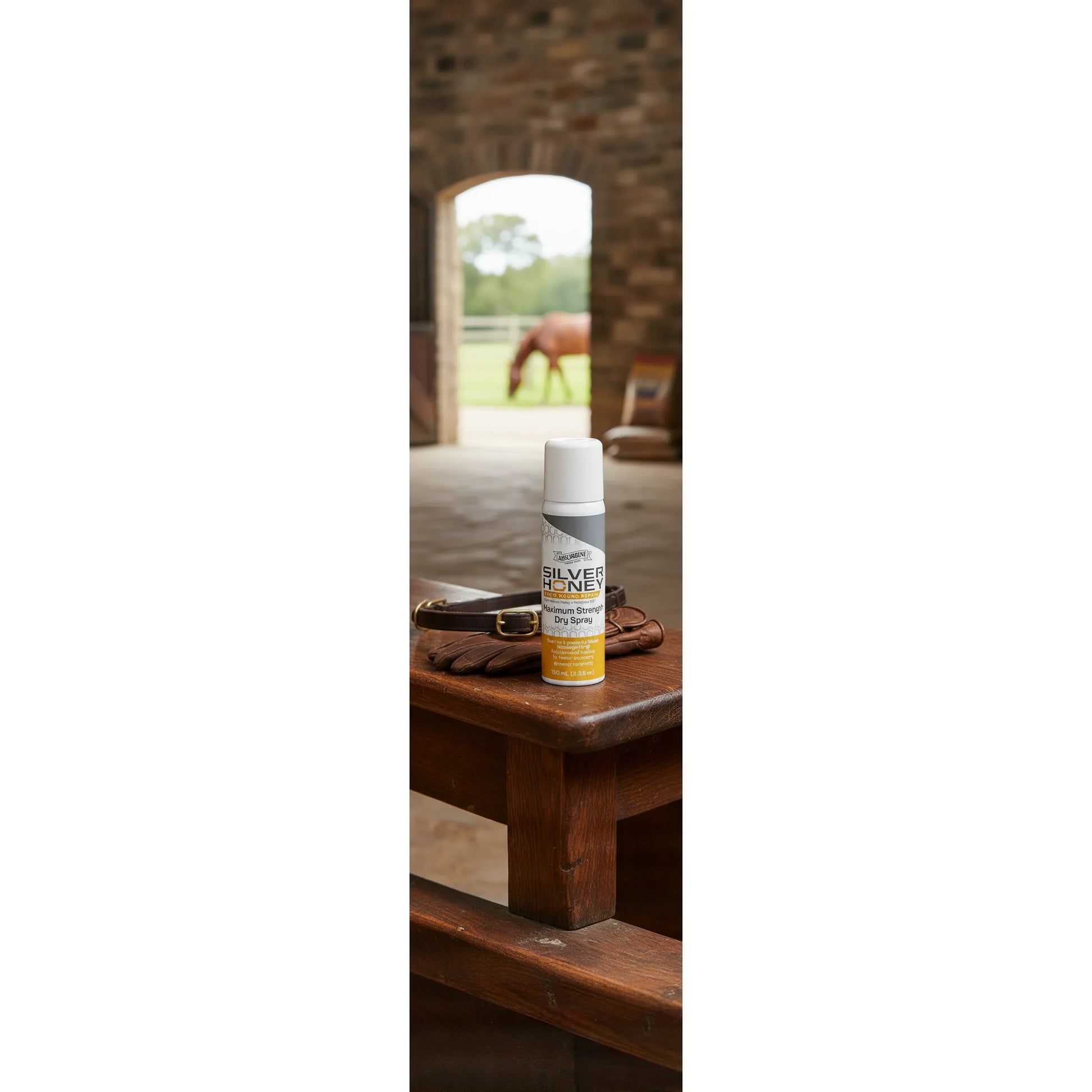 Absorbine Silver Honey Rapid Wound Repair Maximum Strength Dry Spray on a rustic wooden bench with leather tack. In the background, a horse grazes in a green field through a stable door. This medical-grade spray for horses and pets uses Manuka honey and MicroSilver BG for fast healing of cuts and sores. A convenient, no-touch wound care solution for equestrian first aid kits and farm animal supplies.