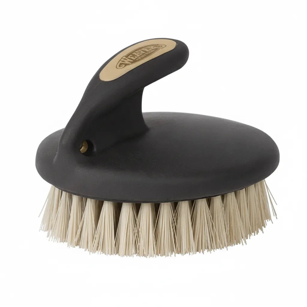 Weaver Leather Palm Brush featuring a contoured black ergonomic handle with a gold logo and soft, dense cream bristles. This professional equine grooming tool is designed for sensitive skin, providing a gentle touch for horse face and body care. The compact, palm-held design ensures maximum control and comfort during stable grooming sessions, making it an essential addition to any equestrian tack box.